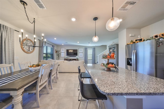 kitchen with hanging light fixtures, stainless steel refrigerator with ice dispenser, a kitchen bar, light tile patterned floors, and light stone counters