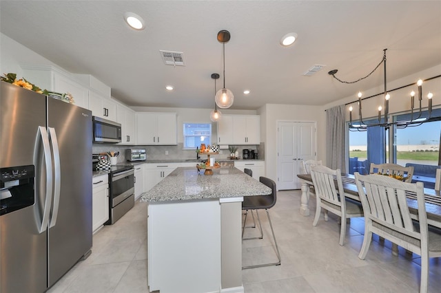 kitchen with appliances with stainless steel finishes, a center island, a wealth of natural light, white cabinets, and a notable chandelier