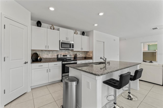 kitchen with sink, tasteful backsplash, an island with sink, stainless steel appliances, and white cabinets