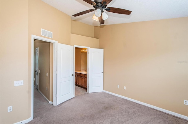 unfurnished bedroom with ensuite bathroom, ceiling fan, light carpet, and a high ceiling