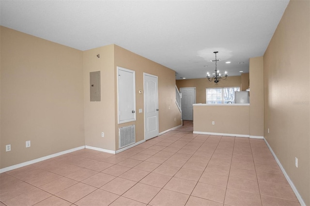 tiled spare room featuring electric panel and a notable chandelier