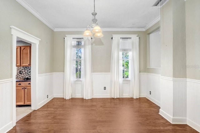 unfurnished dining area with dark wood-type flooring, crown molding, and an inviting chandelier