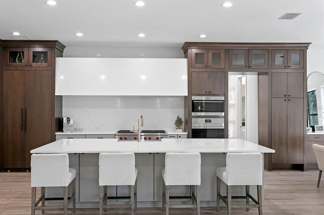 kitchen with a breakfast bar, a kitchen island with sink, and light hardwood / wood-style flooring