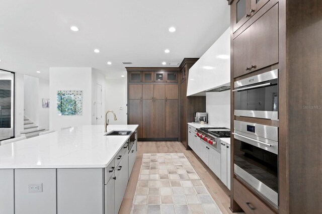 kitchen featuring white cabinetry, a large island, custom exhaust hood, stainless steel gas stovetop, and light hardwood / wood-style flooring