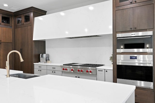 kitchen with sink, light stone countertops, dark brown cabinetry, appliances with stainless steel finishes, and tasteful backsplash