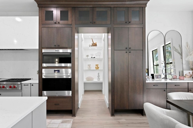 kitchen with light stone counters, appliances with stainless steel finishes, light hardwood / wood-style flooring, and dark brown cabinets