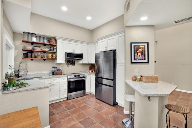 kitchen with appliances with stainless steel finishes, kitchen peninsula, white cabinets, and a breakfast bar area