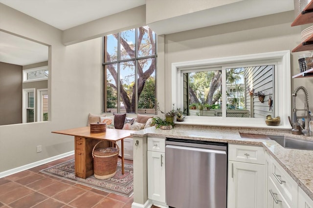 kitchen featuring light stone counters, white cabinetry, stainless steel dishwasher, dark tile patterned flooring, and sink