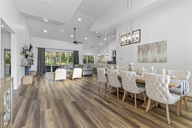 dining room with dark wood-type flooring, ceiling fan with notable chandelier, and high vaulted ceiling