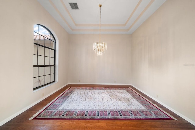 unfurnished room featuring a raised ceiling, wood-type flooring, and a chandelier