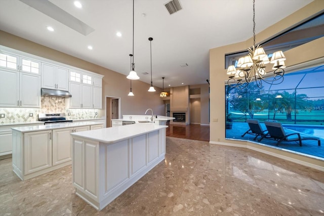 kitchen featuring tasteful backsplash, stainless steel range oven, hanging light fixtures, white cabinets, and a kitchen island with sink