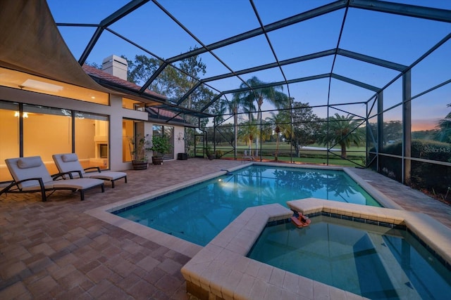 pool at dusk with an in ground hot tub, a patio area, and glass enclosure