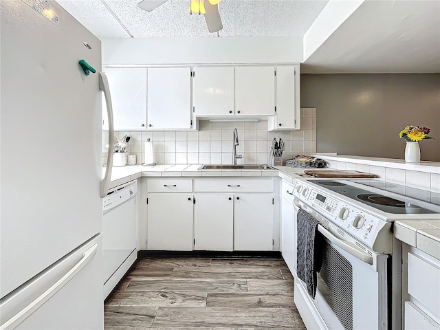 kitchen with white appliances, backsplash, dark wood-type flooring, white cabinets, and sink