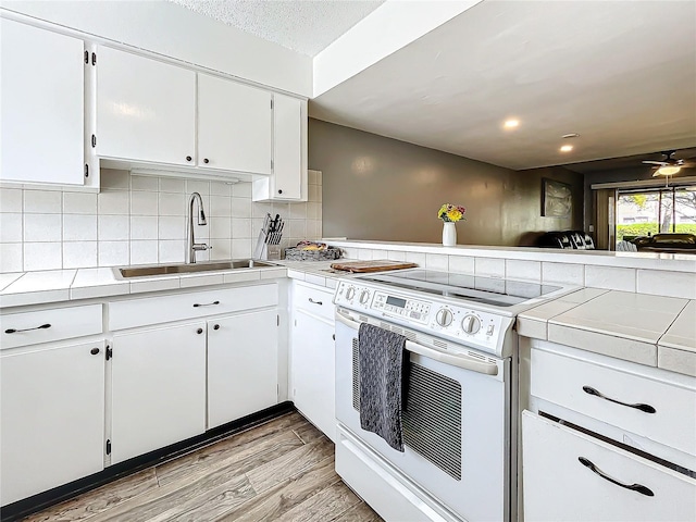 kitchen with tile counters, sink, light hardwood / wood-style flooring, white range with electric cooktop, and white cabinets