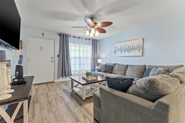 living room with ceiling fan, a textured ceiling, and light wood-type flooring