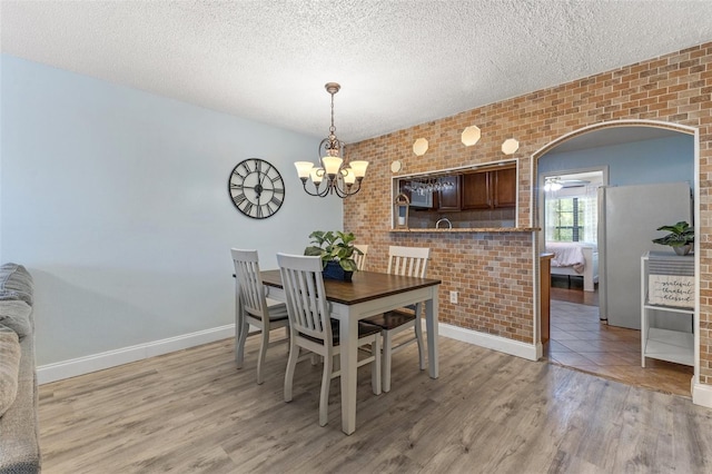 dining area with light hardwood / wood-style floors, a textured ceiling, and brick wall