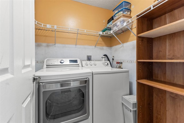 washroom with washing machine and clothes dryer, a textured ceiling, and tile walls