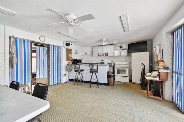 kitchen featuring kitchen peninsula, ceiling fan, a kitchen breakfast bar, white cabinetry, and white appliances