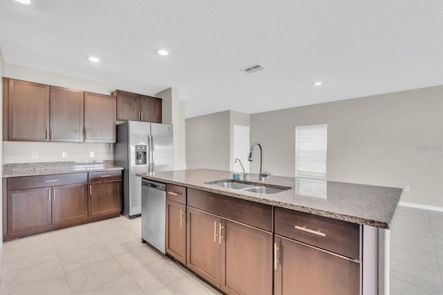 kitchen featuring dark brown cabinets, a center island with sink, stone countertops, stainless steel appliances, and sink