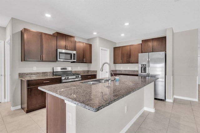 kitchen with a center island with sink, dark stone counters, light tile patterned flooring, sink, and stainless steel appliances