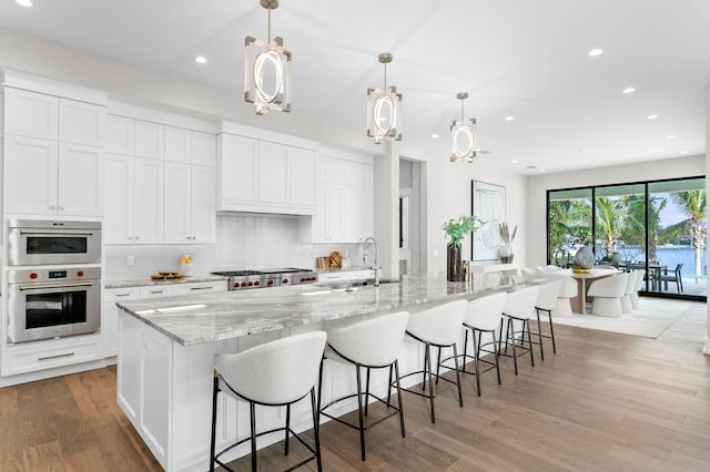 kitchen with white cabinetry, pendant lighting, and a large island with sink