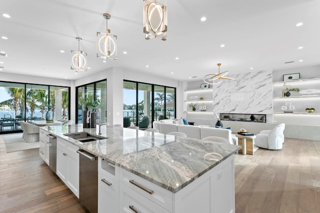 kitchen featuring a large island with sink, sink, white cabinets, and decorative light fixtures