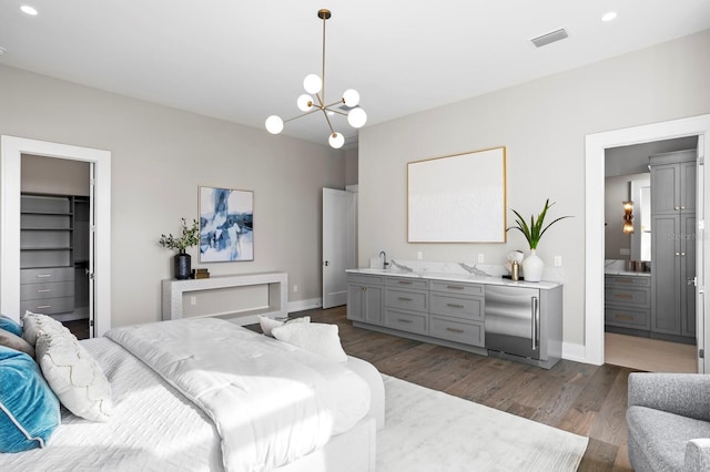 bedroom featuring dark wood-type flooring, stainless steel built in refrigerator, connected bathroom, a notable chandelier, and a spacious closet