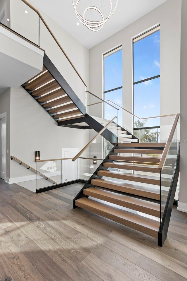 stairs featuring plenty of natural light, a towering ceiling, hardwood / wood-style floors, and an inviting chandelier