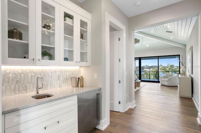 bar with sink, white cabinetry, light wood-type flooring, light stone countertops, and decorative backsplash