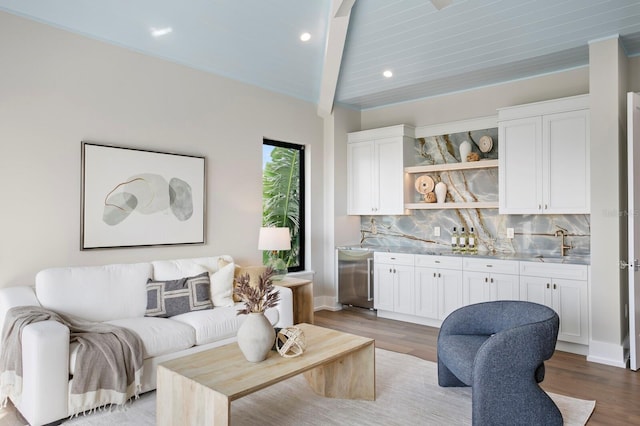 living room featuring beamed ceiling, indoor wet bar, and light hardwood / wood-style flooring