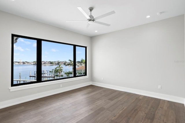 empty room featuring a water view, ceiling fan, and hardwood / wood-style flooring