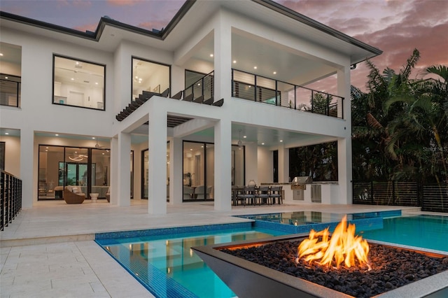 back house at dusk featuring a patio, a balcony, area for grilling, an outdoor fire pit, and a fenced in pool