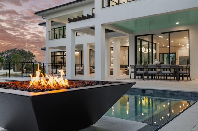 pool at dusk with a patio and a fire pit