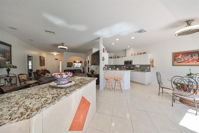 kitchen with decorative backsplash, a kitchen bar, light tile patterned floors, white cabinets, and light stone counters