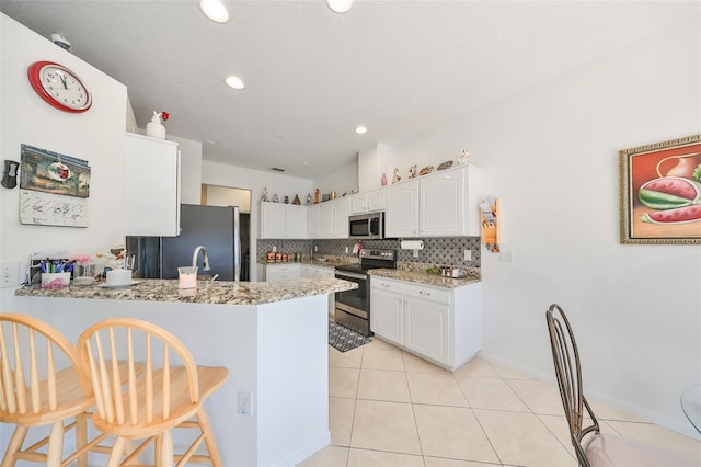 kitchen with appliances with stainless steel finishes, backsplash, kitchen peninsula, a kitchen breakfast bar, and white cabinets