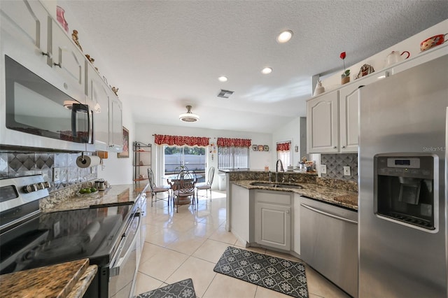 kitchen featuring backsplash, dark stone countertops, sink, white cabinetry, and appliances with stainless steel finishes