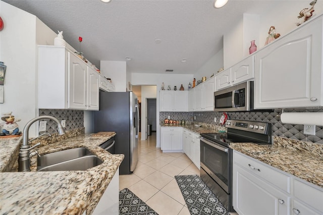 kitchen featuring white cabinets, appliances with stainless steel finishes, a textured ceiling, light stone countertops, and sink