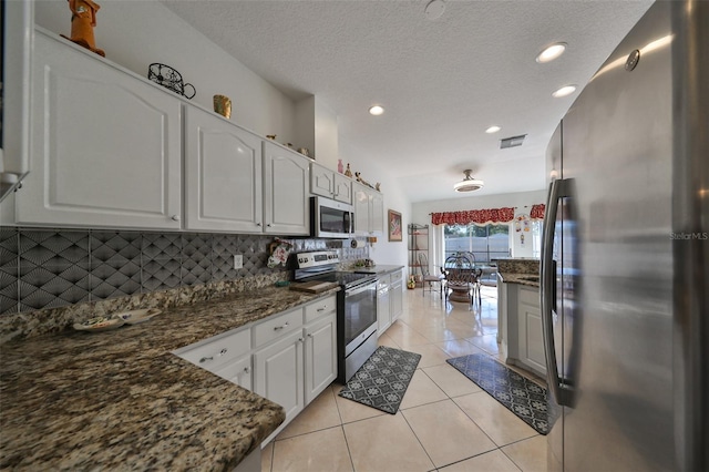 kitchen featuring lofted ceiling, white cabinets, light tile patterned floors, dark stone counters, and stainless steel appliances