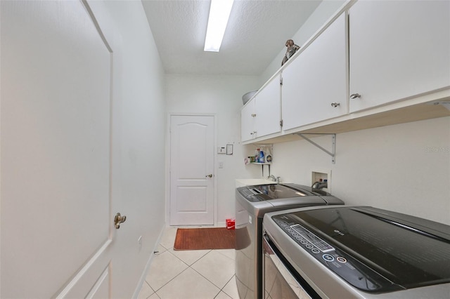 clothes washing area with light tile patterned flooring, a textured ceiling, cabinets, and washing machine and clothes dryer