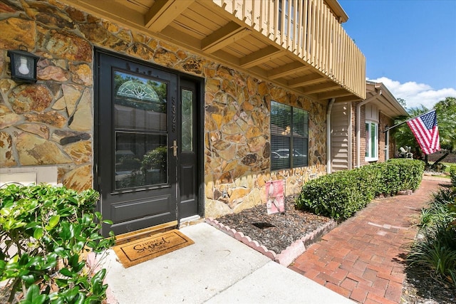 view of exterior entry with stone siding and a balcony