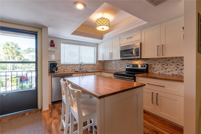 kitchen with a tray ceiling, stainless steel appliances, a center island, white cabinets, and butcher block countertops