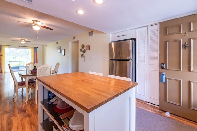 kitchen with white cabinets, ceiling fan, light wood-type flooring, and stainless steel fridge