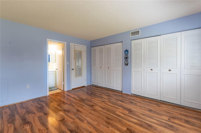 unfurnished bedroom with ensuite bath, a textured ceiling, and dark hardwood / wood-style flooring