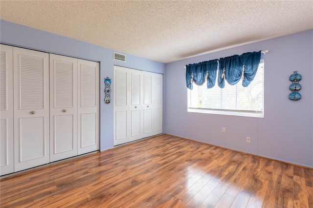 unfurnished bedroom with hardwood / wood-style floors, two closets, and a textured ceiling