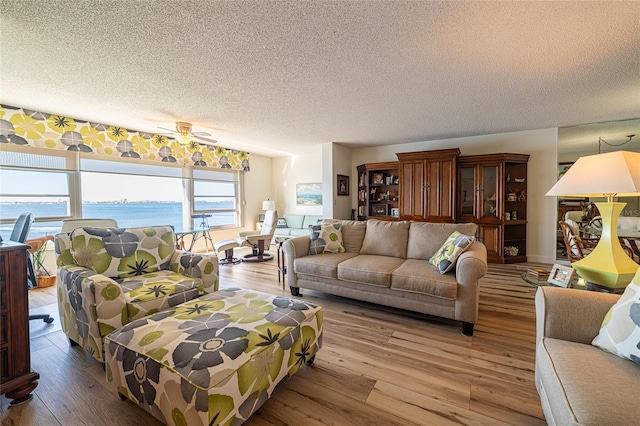 living room featuring a water view, light hardwood / wood-style floors, a textured ceiling, and ceiling fan