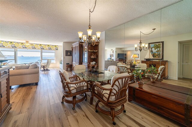 dining space with a water view, a notable chandelier, a textured ceiling, and light wood-type flooring