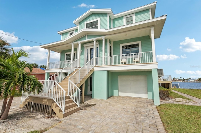 coastal inspired home with a water view, covered porch, and a garage