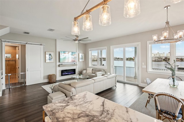 living room featuring ceiling fan with notable chandelier, a water view, dark hardwood / wood-style flooring, and a barn door