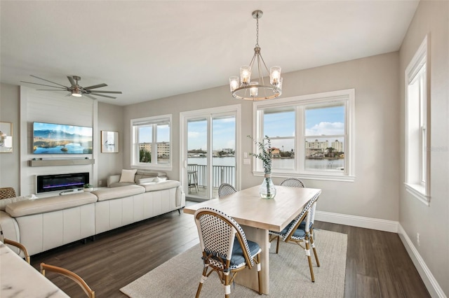 dining area featuring a water view, a wealth of natural light, dark hardwood / wood-style floors, and ceiling fan with notable chandelier