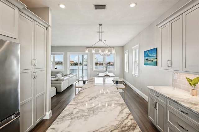 interior space featuring light stone counters, a healthy amount of sunlight, stainless steel refrigerator, and decorative backsplash